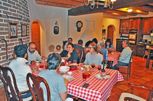A group of people enjoying a meal together at a cozy dining table in a rustic kitchen setting.