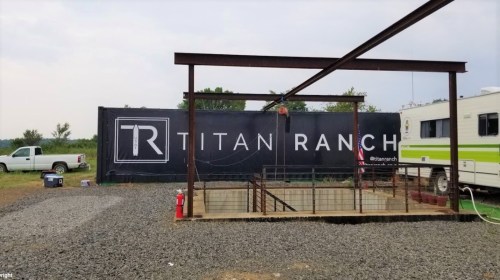 A gravel area with a metal frame structure and a large Titan Ranch banner in the background, alongside a parked RV.