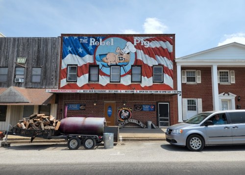 A restaurant called "The Rebel Pig" with a mural of a pig and American flag, featuring a trailer and parked van outside.