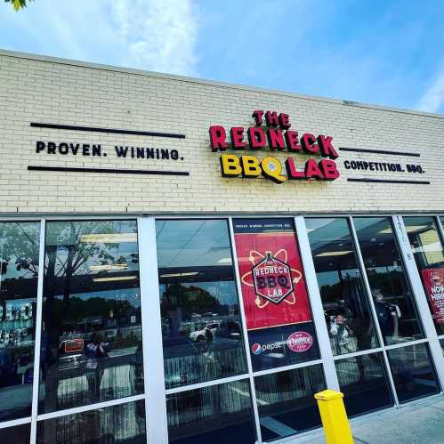 Exterior of The Redneck BBQ Lab, featuring a sign that reads "Proven. Winning. Competition BBQ." and large windows.