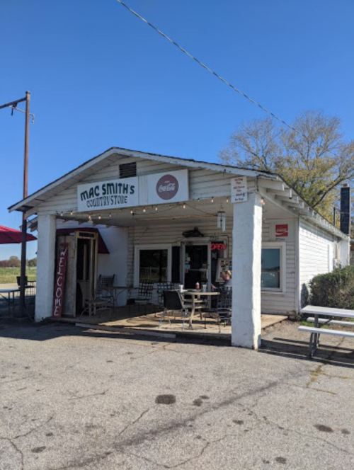 A small, white country store with a sign reading "Mac Smith's," featuring outdoor seating and a welcoming atmosphere.