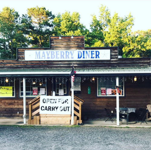 A rustic diner named "Mayberry Diner" with a sign saying "Open for Carry Out" and outdoor seating.