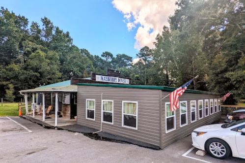A rustic diner with a green roof, surrounded by trees, featuring American flags and a welcoming porch.