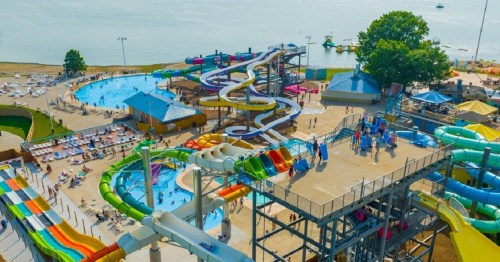 Aerial view of a water park with colorful slides, pools, and people enjoying the sunny day by the water.