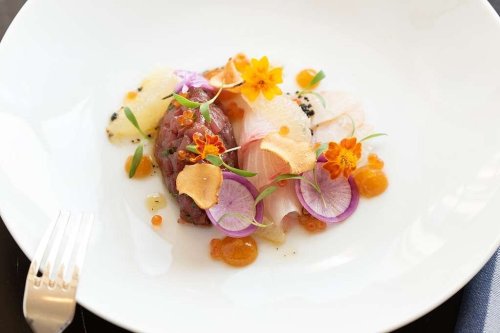 A beautifully plated dish featuring fish, edible flowers, and colorful garnishes on a white plate.