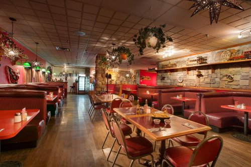Cozy restaurant interior with red booths, wooden tables, and decorative plants, featuring warm lighting and a rustic vibe.