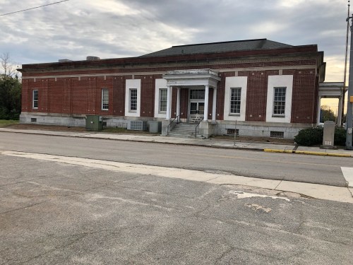 Historic brick building with a prominent entrance, set on a quiet street under a cloudy sky.