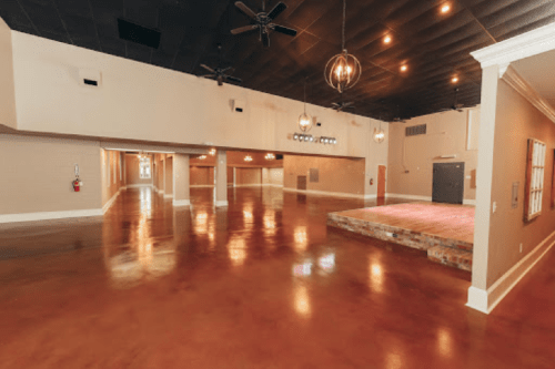 Spacious event venue with polished floors, stage, and modern lighting fixtures.
