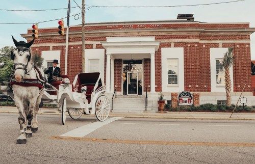 A horse-drawn carriage in front of a historic post office building with red brick and white columns.