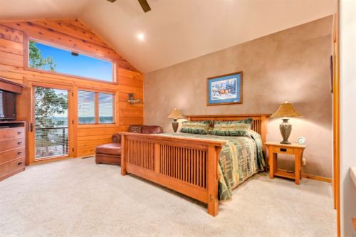 Cozy bedroom with wooden accents, large windows, a comfortable bed, and a leather chair, featuring warm lighting.