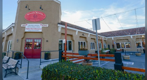 Exterior of Running Rooster restaurant with a sign for take-out dinners, featuring a warm, inviting design.