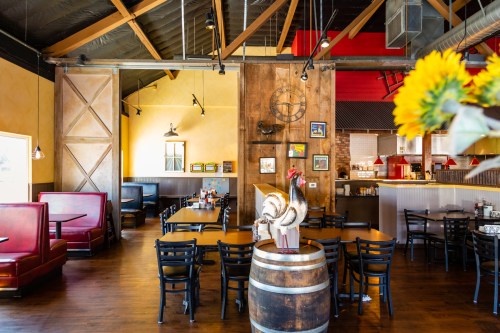 Cozy restaurant interior with wooden accents, red booths, and a decorative rooster on a barrel. Sunflower in the foreground.