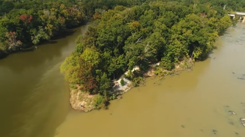 Aerial view of a lush green island surrounded by muddy rivers and trees, with a small beach area visible.