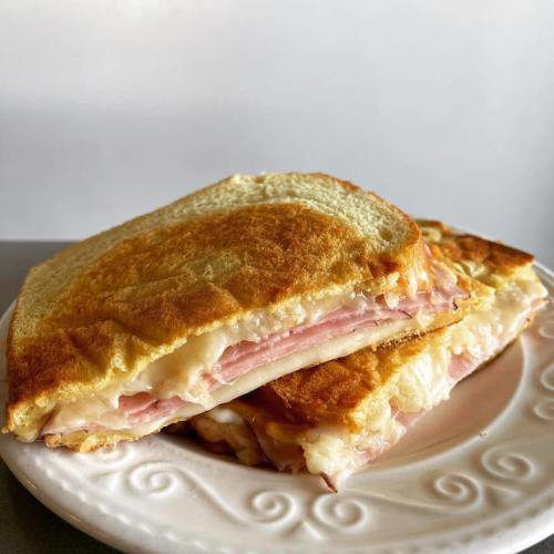 A golden-brown grilled sandwich with layers of ham and melted cheese, served on a decorative white plate.