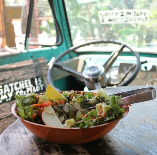 A colorful salad in a bowl with fresh vegetables, set on a rustic table inside a vintage vehicle.