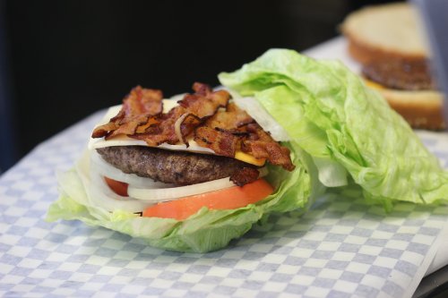 A lettuce-wrapped burger with bacon, cheese, tomato, and onion, served on a checkered paper.