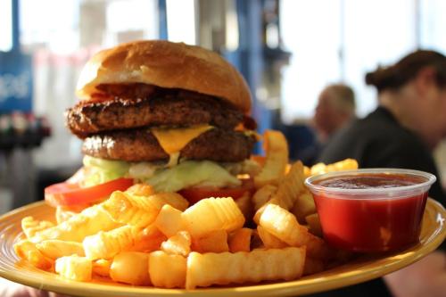 A large burger with two patties, cheese, lettuce, and tomato, served with a side of crinkle-cut fries and ketchup.