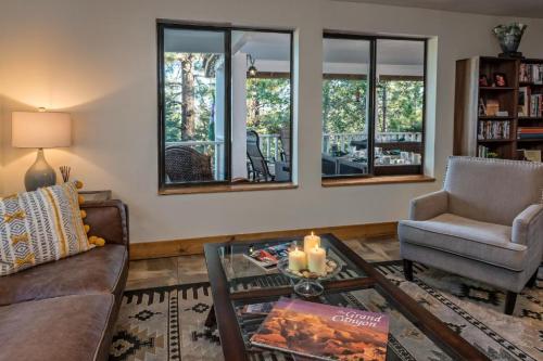 Cozy living room with a sofa, armchair, coffee table, candles, and large windows overlooking a forested area.