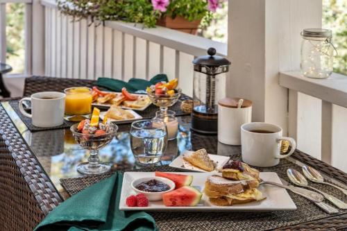 A beautifully set breakfast table with pancakes, fruit, coffee, and juice, surrounded by greenery and flowers.