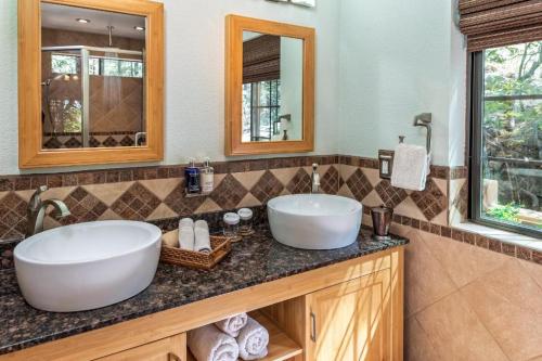 Modern bathroom with dual vessel sinks, wooden cabinetry, and natural light from a window. Decorated with towels and toiletries.