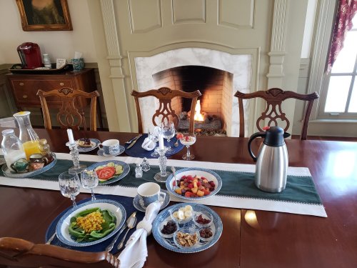 A beautifully set dining table with a variety of breakfast foods, a cozy fireplace in the background.
