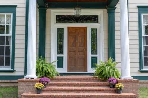 A welcoming front porch with a wooden door, white columns, and potted flowers on brick steps.