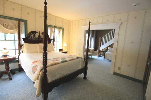 Cozy bedroom with a four-poster bed, patterned quilt, and soft lighting, featuring vintage decor and a staircase in the background.