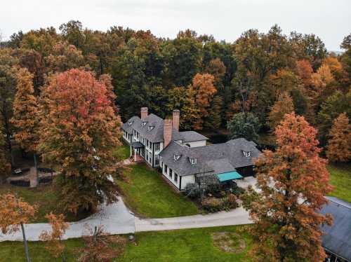 Aerial view of a large house surrounded by vibrant autumn trees in a wooded area.