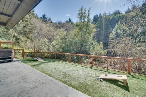 A sunny outdoor patio with a grassy area, surrounded by trees and a wooden railing.