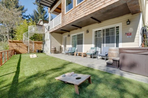 A cozy outdoor patio with seating, a hot tub, and a lawn area, surrounded by trees and a spiral staircase.