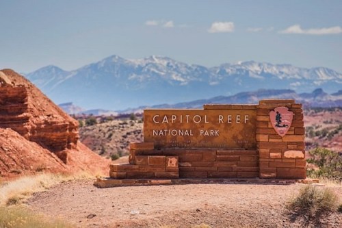 Sign for Capitol Reef National Park with mountains in the background and red rock formations in the foreground.