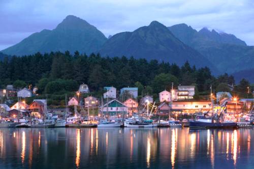 A serene harbor at dusk, with boats docked and mountains in the background, illuminated by soft lights from nearby buildings.