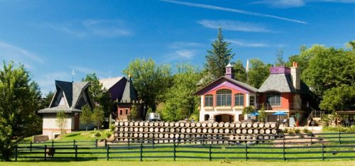 A picturesque landscape featuring unique houses and stacked logs, surrounded by lush greenery under a clear blue sky.