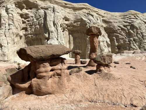 Unique rock formations with mushroom-like shapes against a backdrop of light-colored cliffs and a clear blue sky.