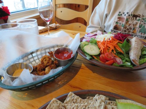 A table setting with a salad, fried food, dipping sauce, and drinks in a cozy restaurant.