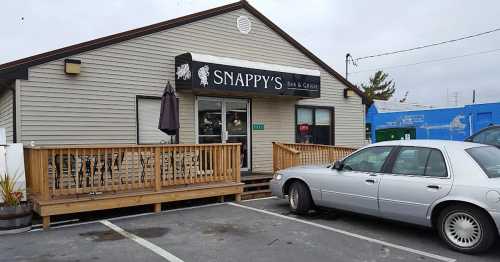 Exterior of Snappy's Bar & Grille, featuring a wooden deck and a parked car in front. Overcast sky in the background.