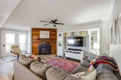 Cozy living room with a gray sofa, wooden accent wall, TV unit, and a colorful rug, featuring natural light from windows.