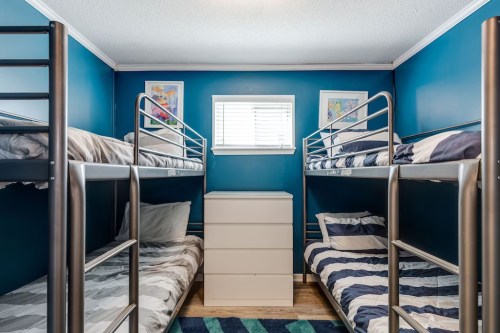 A cozy room with two sets of metal bunk beds, a white dresser, and blue walls adorned with colorful artwork.