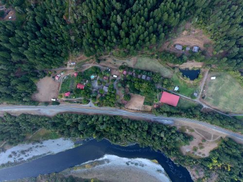 Aerial view of a rural area with a river, green trees, and several buildings scattered throughout the landscape.