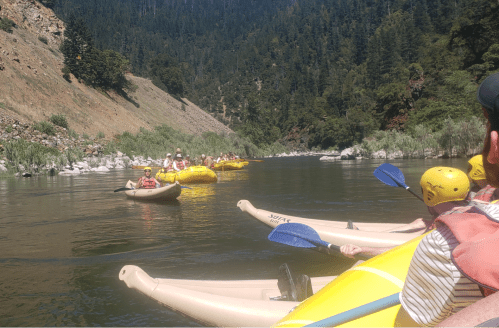 A group of people kayaking on a calm river surrounded by lush greenery and steep hills.
