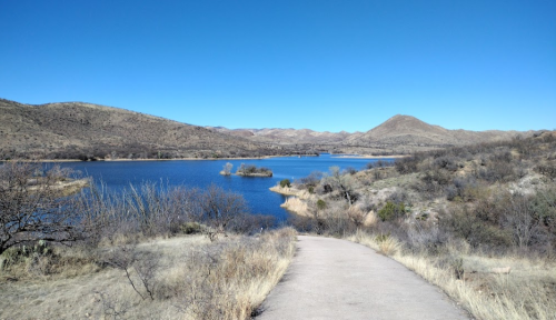 A serene landscape featuring a lake surrounded by hills and sparse vegetation under a clear blue sky.