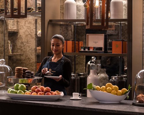 A barista serves pastries at a stylish café, surrounded by fresh fruits and elegant decor.