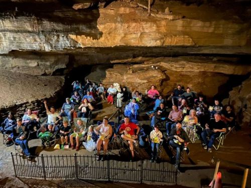 A large group of people seated in folding chairs inside a cave, enjoying an event under natural rock formations.