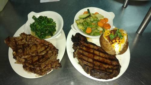 A plate with grilled steak, a baked potato topped with sour cream, and sides of sautéed vegetables and greens.