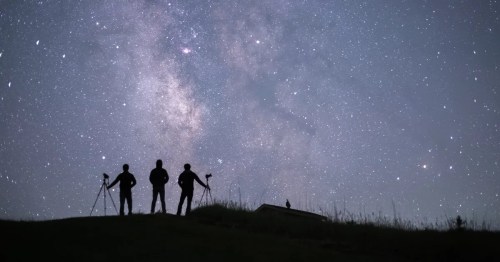 Silhouettes of three photographers against a starry night sky with the Milky Way visible.