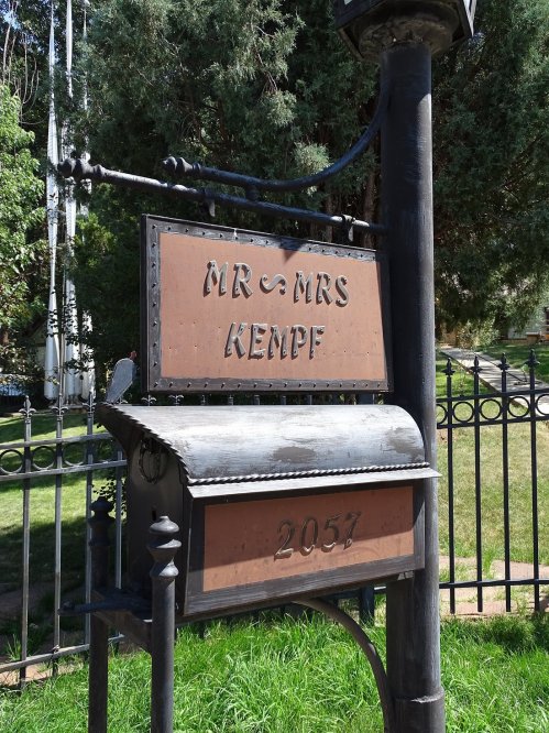 A decorative mailbox with the names "Mr. & Mrs. Kempf" and the number "2057" on a post in a green yard.