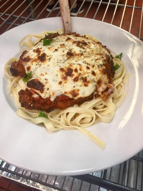 A plate of fettuccine topped with breaded chicken, marinara sauce, and melted cheese, garnished with parsley.