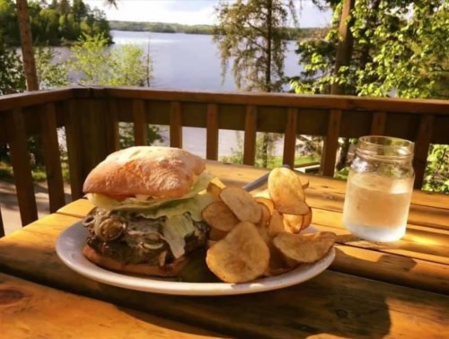 A delicious burger with lettuce and pickles, served with potato chips and a glass of water, by a scenic lakeside.