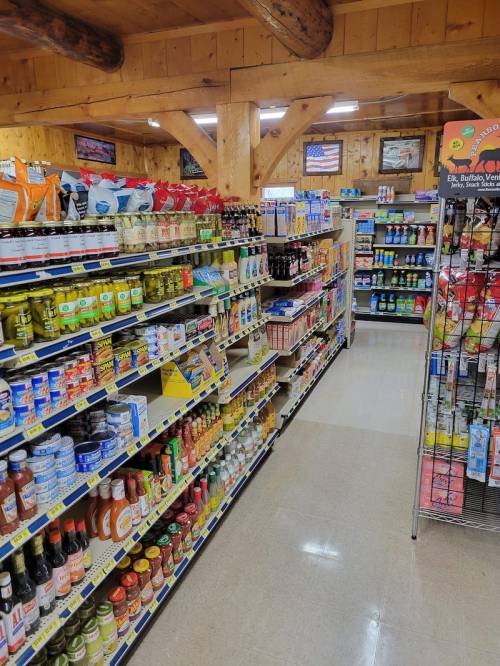 A grocery store aisle filled with various food products, including sauces, canned goods, and snacks on wooden shelves.
