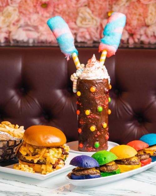 A colorful feast featuring a burger with cheese, fries, and a vibrant milkshake topped with cotton candy and sprinkles.
